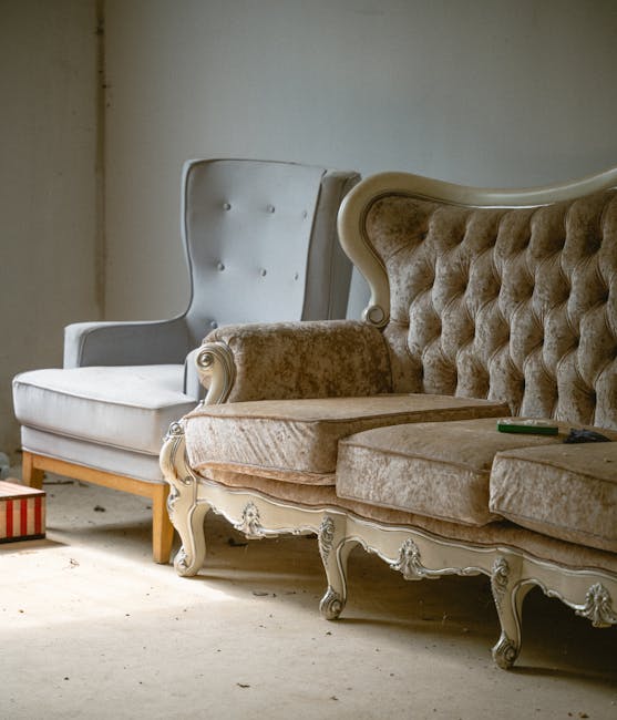 A man with a beard and casual clothing is lifting a small wooden table with a natural wood finish, which is being removed from a living room. The room features white-painted walls and a polished woode